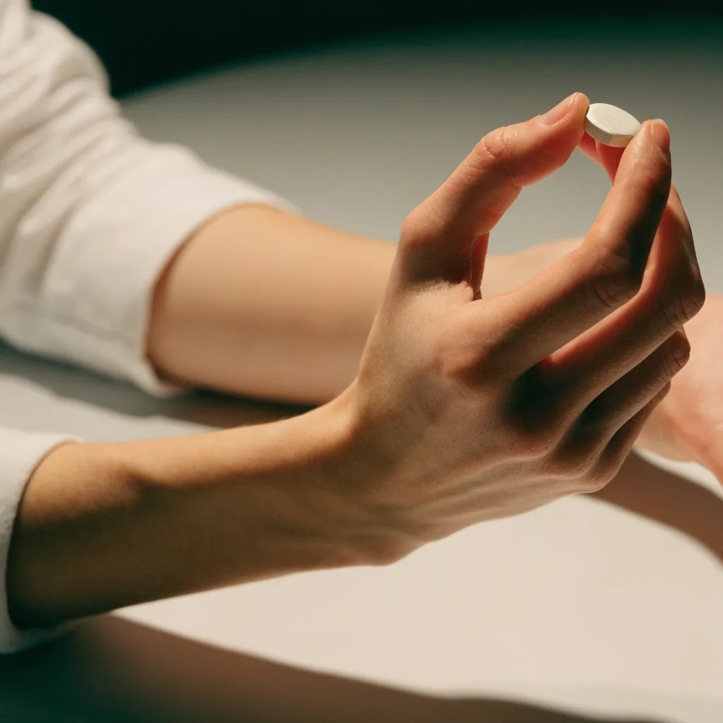 A hand holding a single plain zinc tablet above a matte surface